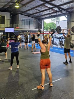 Members pressing barbells overhead during a group class