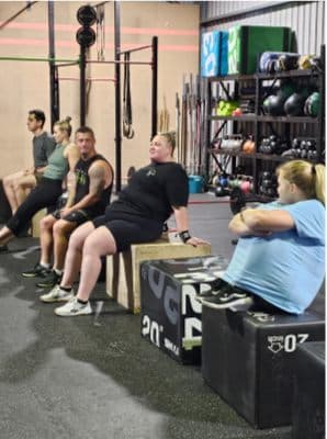 Members resting on plyo boxes between efforts, chatting and laughing