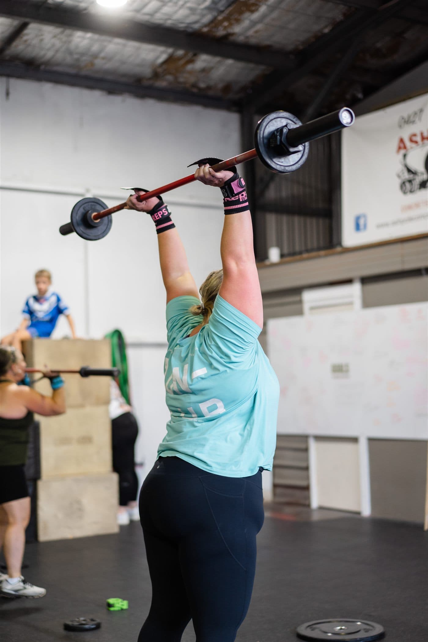 A member holding a barbell locked out overhead